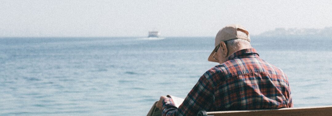 image showing older man sitting on a bench looking out to sea